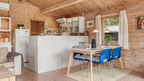 A cozy cabin interior with a wooden interior, a dining area with blue chairs, a kitchen with white cabinets, and a large window with curtains. - "Jannus" - 550m from the sea by Interhome (Hals)