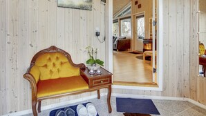 Ein gemütlicher Raum mit Holzvertäfelung, einem komfortablen gelben Sofa, einem kleinen Tisch mit Blumen und Blick in den angrenzenden Wohnbereich.