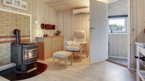 Ein gemütliches Zimmer mit Kaminofen, bequemen Sessel und einem kleinen Tisch.
