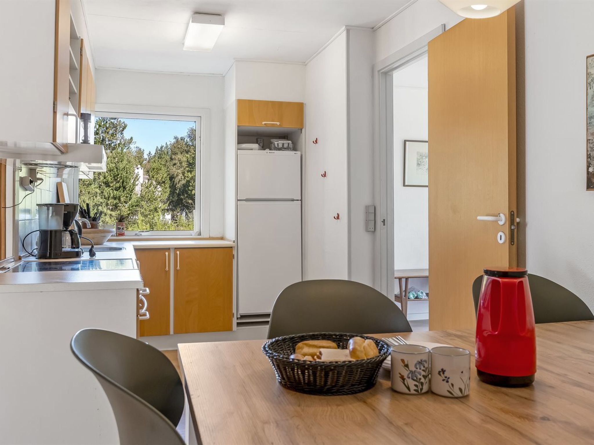 A compact kitchen with a coffee maker, a refrigerator, and a window with a view of trees.
