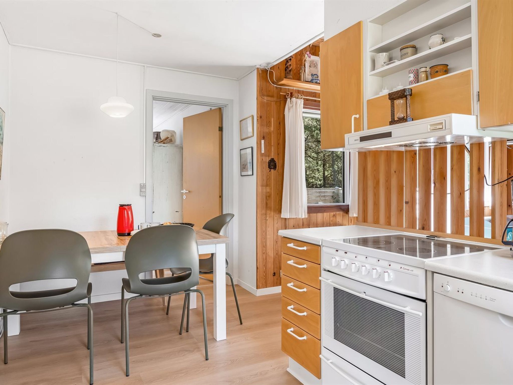 A modern kitchen with wooden cabinets, a built-in oven, and a dining area with two chairs and a table.