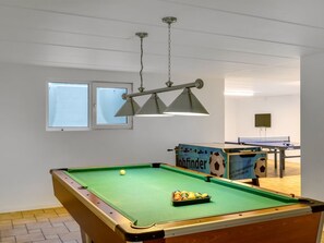 Une table de billard avec une queue et des billes, une table de baby-foot et un luminaire fixé au plafond.