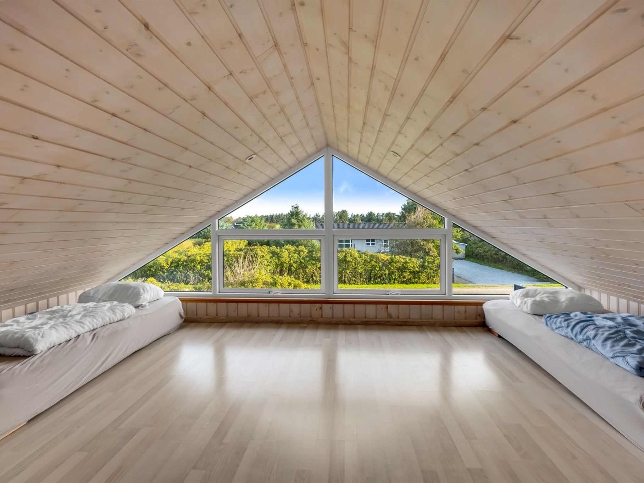 Une pièce avec un plafond en pente, de grandes fenêtres et une vue sur la verdure et un bâtiment à l’extérieur.