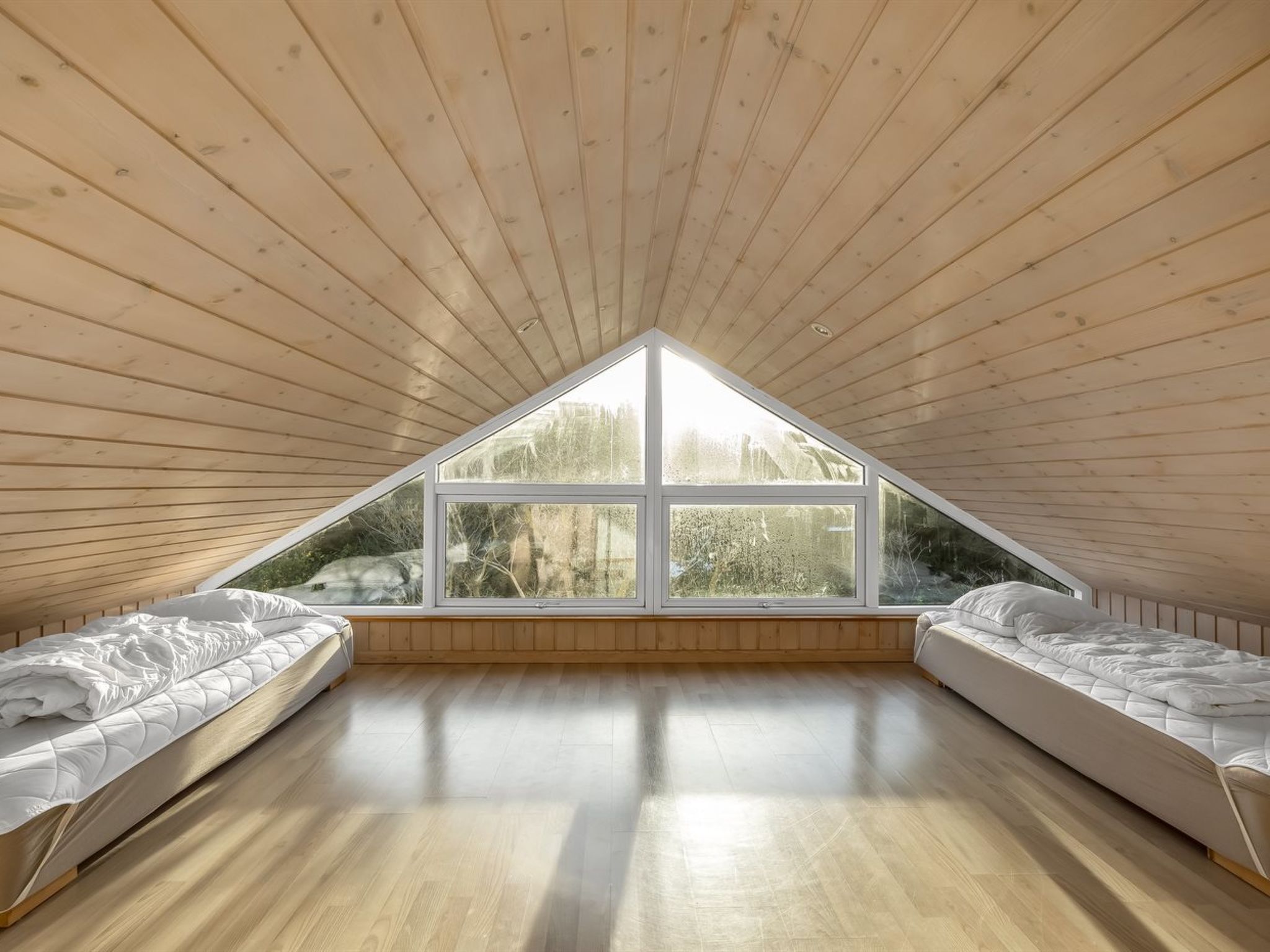 A room with a sloped ceiling and a large window providing a view of trees.