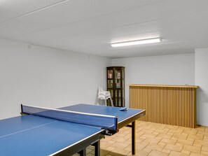 Une pièce avec une table de ping-pong, un radiateur et une porte dotée d’un panneau en verre.