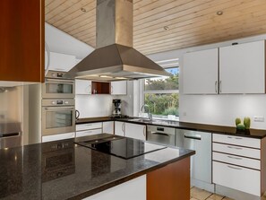 A modern kitchen with a central island, stainless steel appliances, and a view of greenery outside.