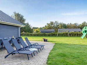 Un espace extérieur aménagé avec des fauteuils de jardin, une pelouse et un terrain de jeux doté d’un toboggan.