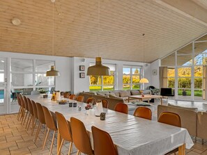 Un vaste espace dédié à la salle à manger, avec une longue table, de nombreuses chaises et des luminaires suspendus.