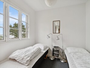 Ein Zimmer mit zwei Einzelbetten, einem Stehpult mit Stuhl, einer Schreibtischlampe, einem Spiegel und einem Fenster mit Blick auf Bäume.
