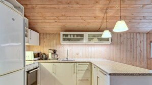 A compact kitchen with wooden paneling, white cabinets, a built-in oven, a microwave, a coffee maker, and a hanging light fixture. - "Elsemaria" - 1.3km from the sea by Interhome (Løkken)