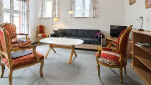 Ein Wohnzimmer mit einer Couch, zwei Sesseln, einem runden Couchtisch und einem Fernseher.