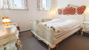 Ein klassisches Schlafzimmer mit einem weißen Bett, aufwendigen Möbeln und blumigen Vorhängen.