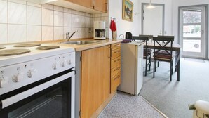 Eine moderne Küche mit Herd, Backofen, Spüle und Holzschränken. Ein Essbereich mit Tisch und Stühlen ist ebenfalls vorhanden.