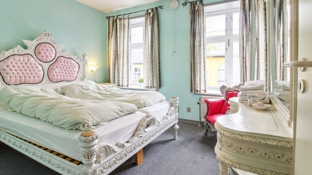Une chambre avec un grand lit, une coiffeuse avec un miroir et une fenêtre avec des rideaux.