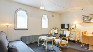 Un salon comprenant un canapé, une petite table, deux fauteuils décoratifs, un téléviseur et une lampe.