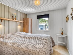 Une chambre à coucher avec un lit, une fenêtre donnant sur un beau paysage, une armoire en bois et une petite table sur laquelle est posé un vase.