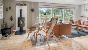 A cozy living room with a fireplace, a sofa, a chair, and a view of the outdoors. - "Gloria" - 2.5km from the sea by Interhome (Blokhus)