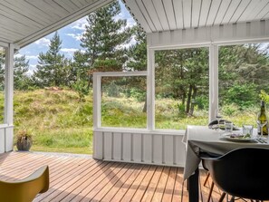 Un espace extérieur abrité, aménagé pour les repas, avec une table pour deux personnes, offrant une vue sur un paysage naturel composé d’arbres et d’herbe.