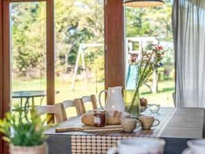 An outdoor dining area with a table set for two, featuring a pitcher, bread, and a vase with flowers.