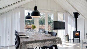 A dining area with a table set for four, large pendant lights, a fireplace, and a TV mounted on the wall.