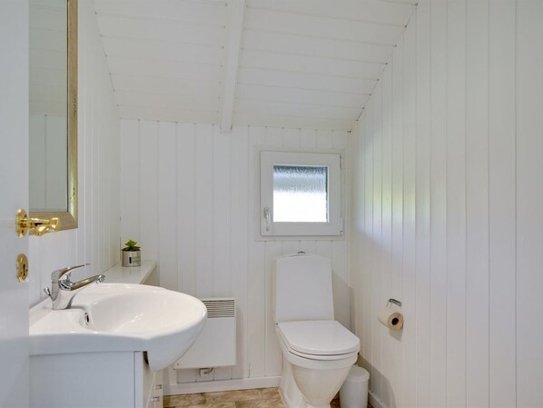Un baño pequeño y blanco con lavamanos, inodoro y ventana sobre el inodoro.