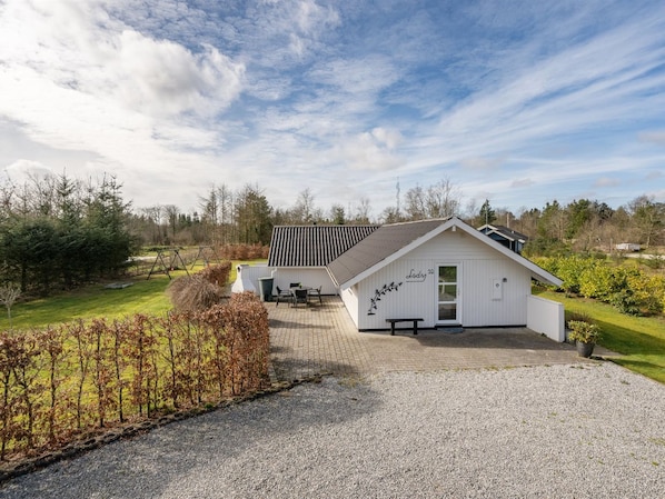 A white building with a sloped roof, a patio with outdoor seating, and a gravel driveway.