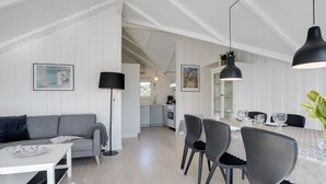 A modern kitchen with white cabinetry, a dining area with a table set for four, and a grey sofa with a book and a plate.