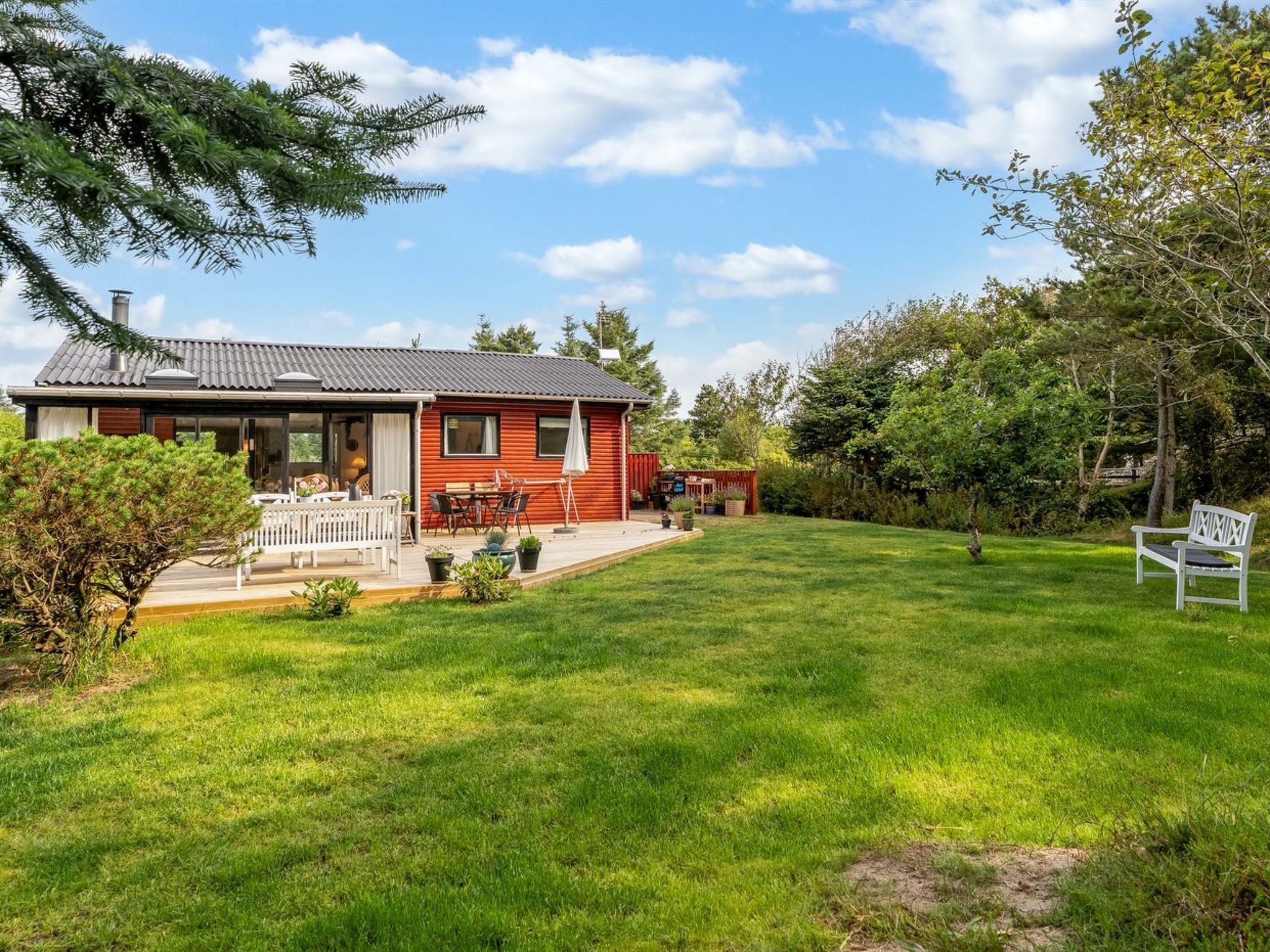 A red house with a covered porch, a lawn, and a bench.