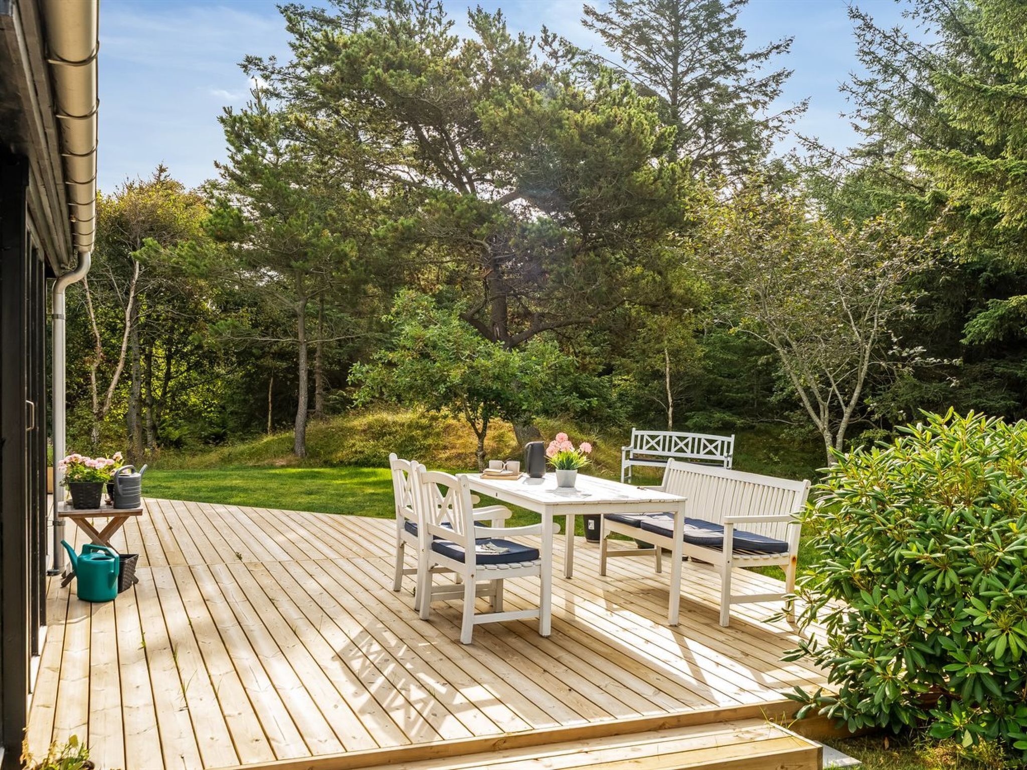 Een houten terras met een tafel en stoelen, omringd door groen en bomen.