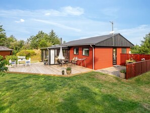 Uma casa de madeira vermelha com varanda, um pátio com móveis de exterior e uma antena parabólica.