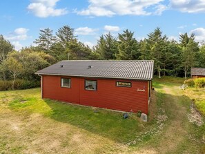 Een rode houten chalet met een metalen dak, omringd door een gazon en bomen.