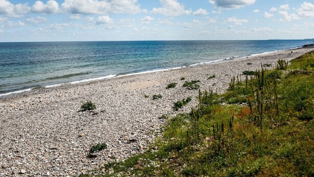 A pebbled beach with a clear view of the sea and a distant shoreline.