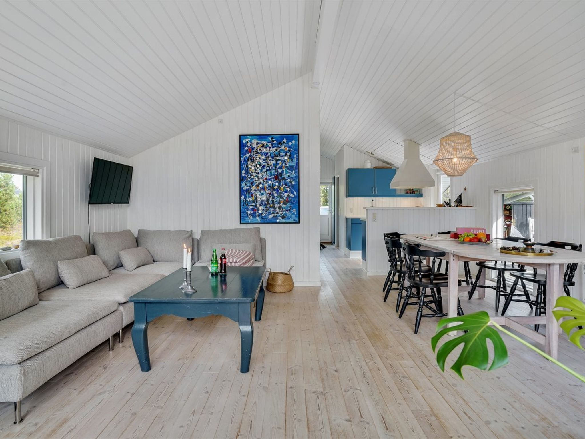 A spacious living area with a sofa, coffee table, and dining table. A large abstract painting adorns the wall, and a kitchen is visible in the background.