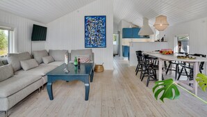 A spacious living area with a sofa, coffee table, and dining table. A large abstract painting adorns the wall, and a kitchen is visible in the background.