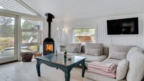 A cozy living room with a wood-burning stove, a sofa, a TV, and a table with a candle and a bottle.