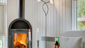 A cozy room with a wood-burning stove, a candle, and a bottle of drink on a table.
