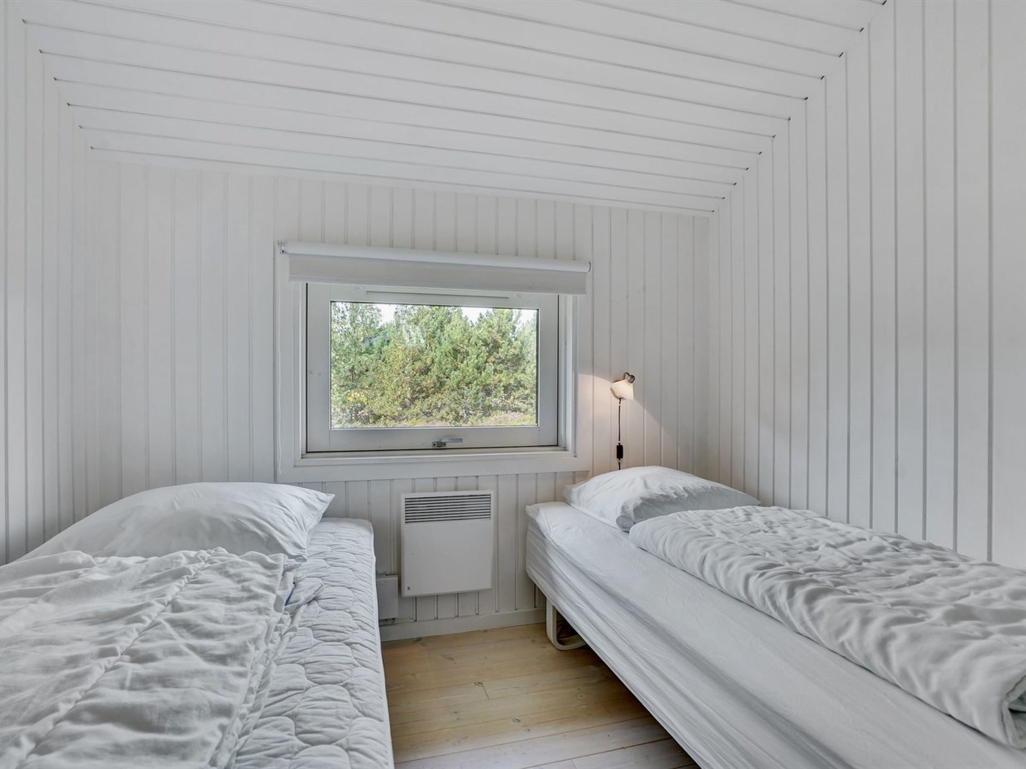 Ein Zimmer mit zwei Einzelbetten, einem Fenster mit Blick auf Bäume, einem Wandheizkörper und einer Nachttischlampe.