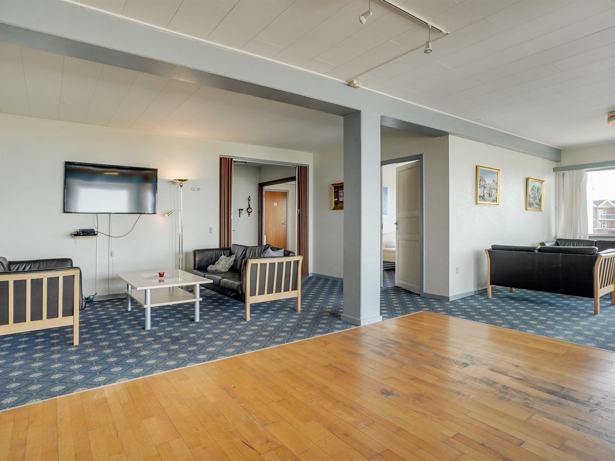 A modern living room with a flat-screen TV, a sofa, a coffee table, and a wooden floor.