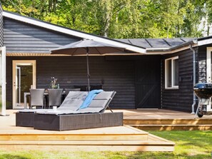 Ein überdachter Außenbereich mit einer Couch, einem Tisch, einem Grill und einer Tür zu einer überdachten Terrasse.