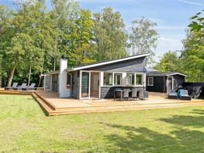 Ein modernes Haus mit Terrasse, Sitzgelegenheiten im Freien und einem großen Fenster mit Blick auf den Garten.