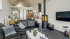 Ein modernes Wohnzimmer mit einem schwarzen Ledersofa, einem weißen Couchtisch mit Kerzen und einem großen, an der Wand montierten Flachbildfernseher.