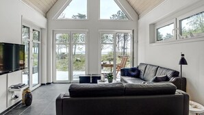 Ein geräumiges Wohnzimmer mit einer großen schwarzen Ledersofa, einem Flachbildfernseher und einem Essbereich mit Tisch und Stühlen.