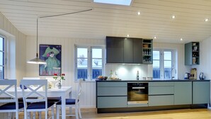 A modern kitchen with a built-in oven, a dining area with white chairs, and a large window providing natural light. - "Sofine" - 250m from the sea by Interhome (Løkken)