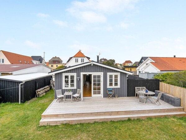 Une maison de plain-pied avec une terrasse, un jardin clôturé et un ciel dégagé.
