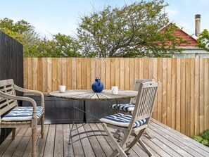 Une terrasse en bois avec une table ronde et deux chaises, une carafe bleue et une tasse blanche.