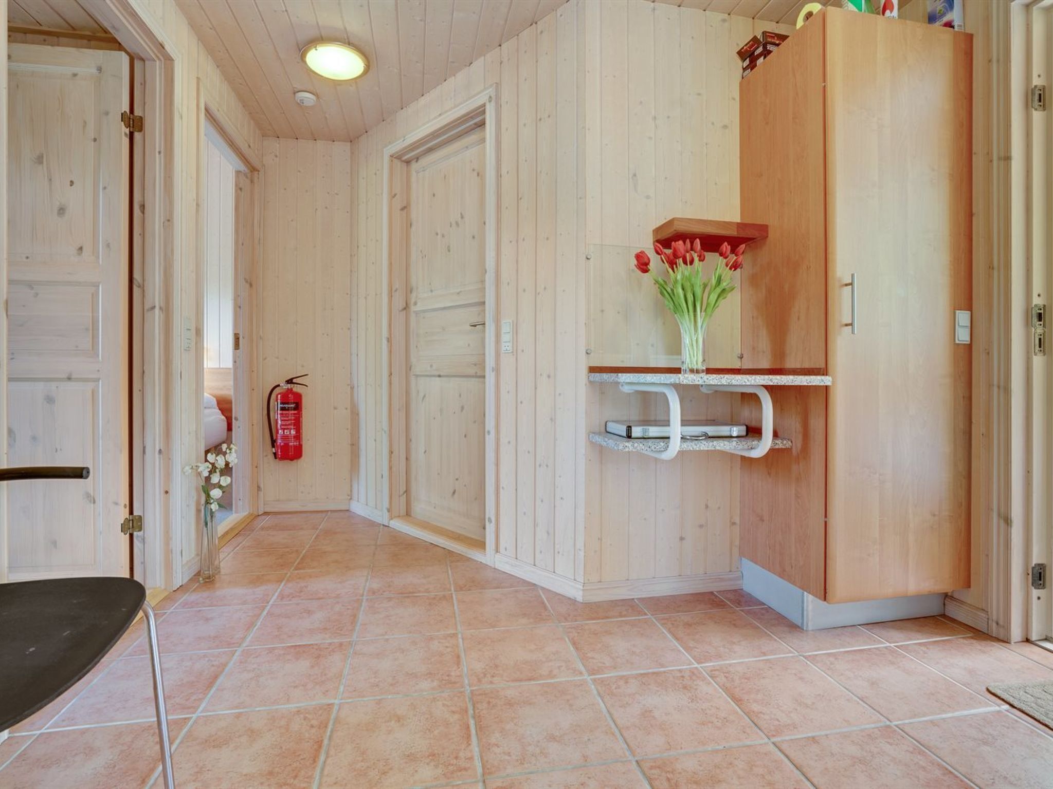 Een houten interieur met een betegelde vloer, een brandblusser en een plank met een bloevas.