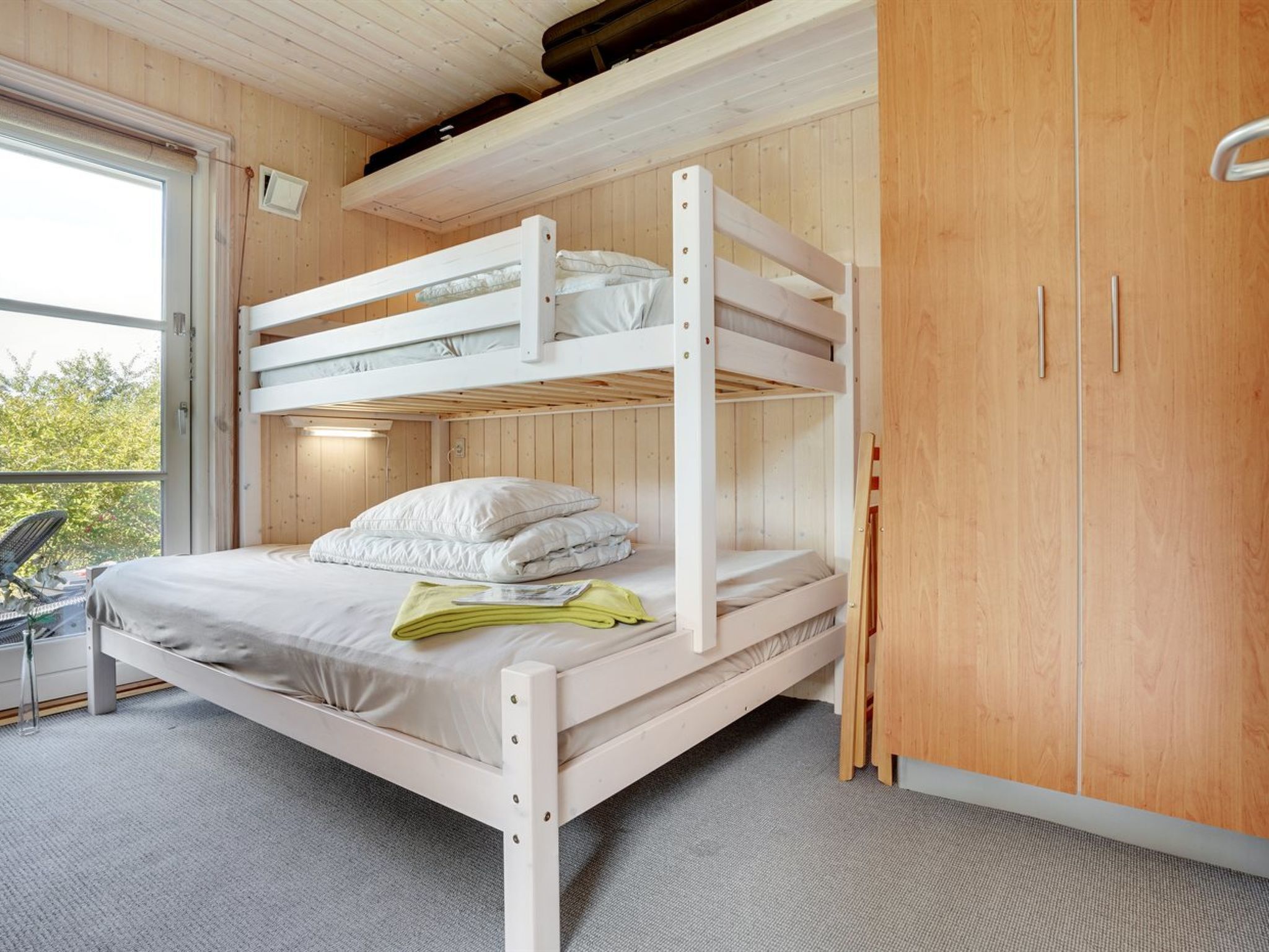 A bunk bed room with a wooden ceiling, a window, and a wardrobe.