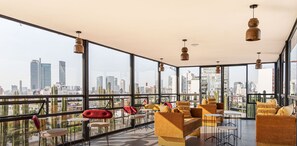 Relax in a spacious lounge with a panoramic city view, featuring comfortable seating and pendant lighting.