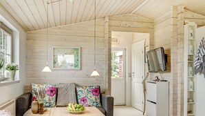 Habitació acollidora amb sostre de fusta, un sofà amb coixinets florals, una taula petita amb un bol de fruita i un televisor fixat a la paret.