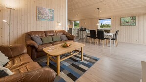 A spacious living area with a brown leather sofa, a wooden coffee table, and a dining table with chairs. The room has wooden walls and a high ceiling. - "Clement" - 500m to the fjord by Interhome (Skjern)